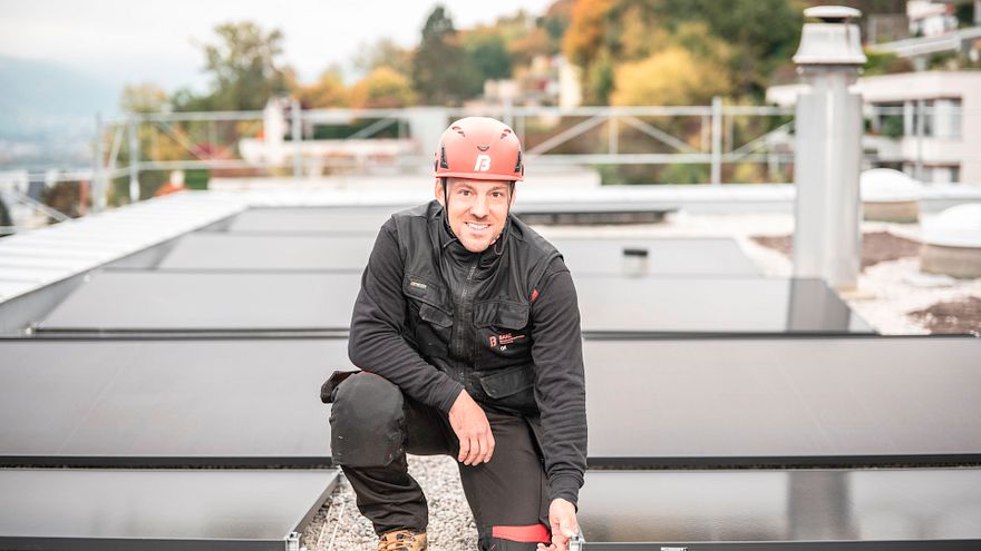Dachdecker Mischa vor Photovoltaik-Anlage auf dem Dach, knieend.