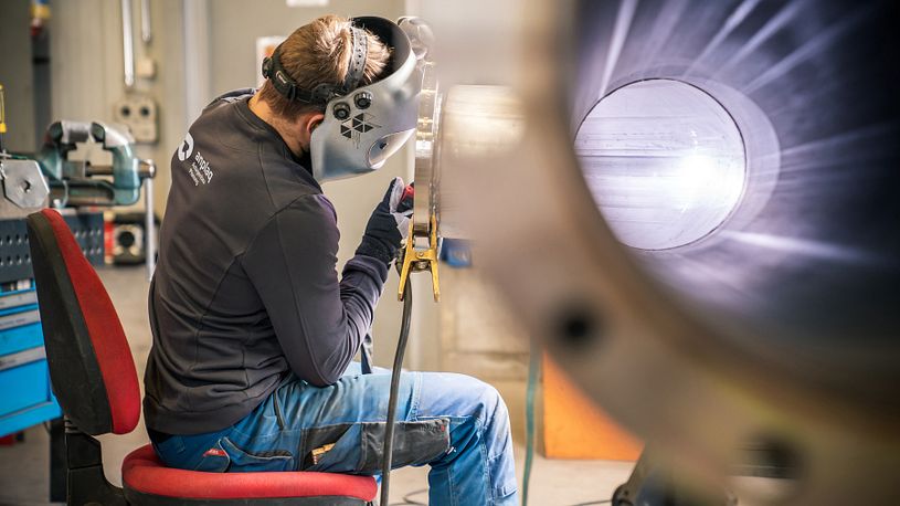Mitarbeiter bearbeitet ein zylindrisches Metallbauteil